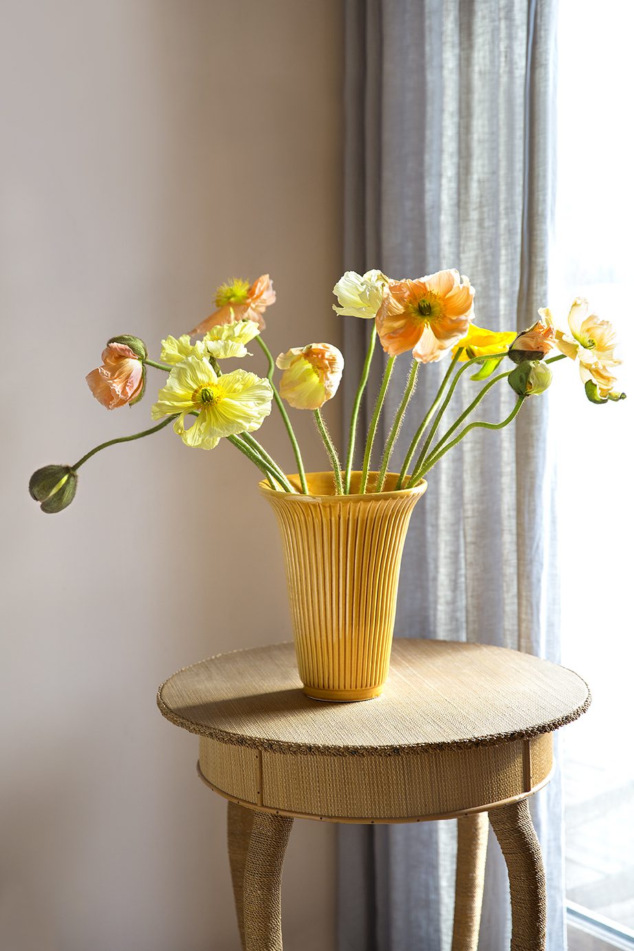 Yellow glazed vase with yellow flowers on a stool.