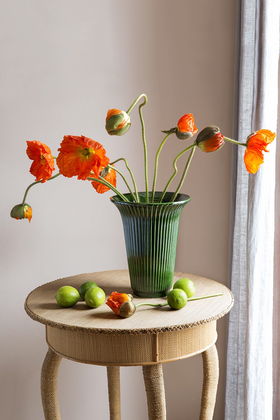 Green vase with large orange flowers on a stool.