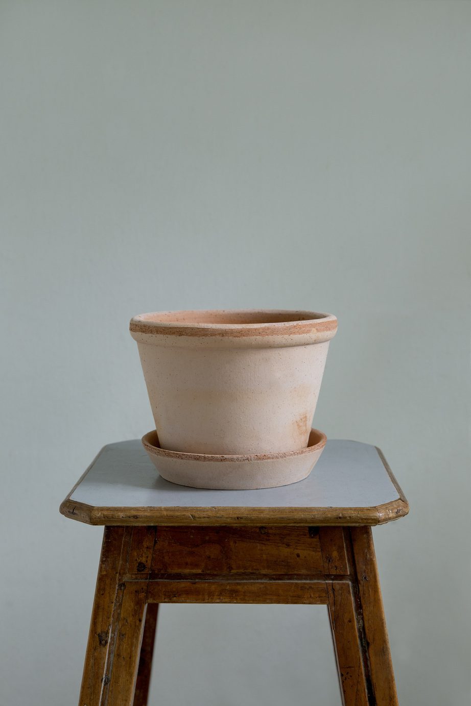 Raw rose terracotta pot with saucer on a stool.