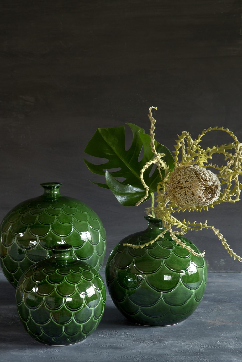 Three green glazed round-shaped vases with a pattern of petals.