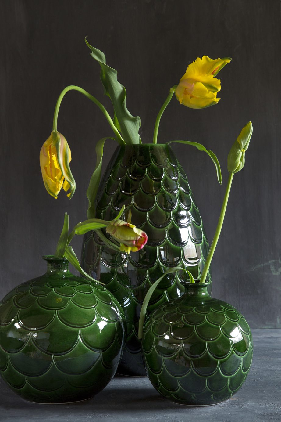 Two round-shaped and one cone-shaped green glazed vases with flowers.