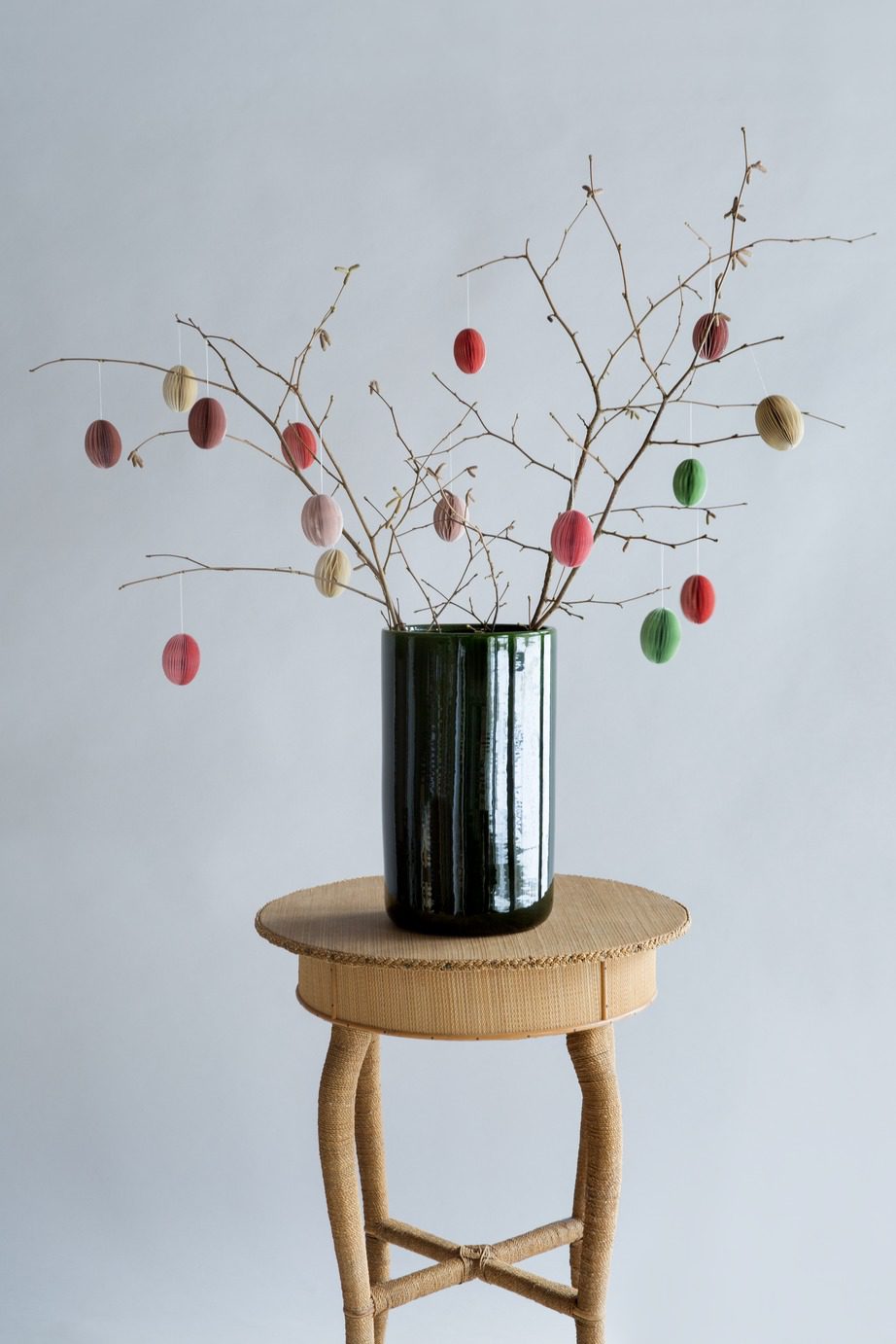 Simple green glazed vase with branches and easter eggs on a stool