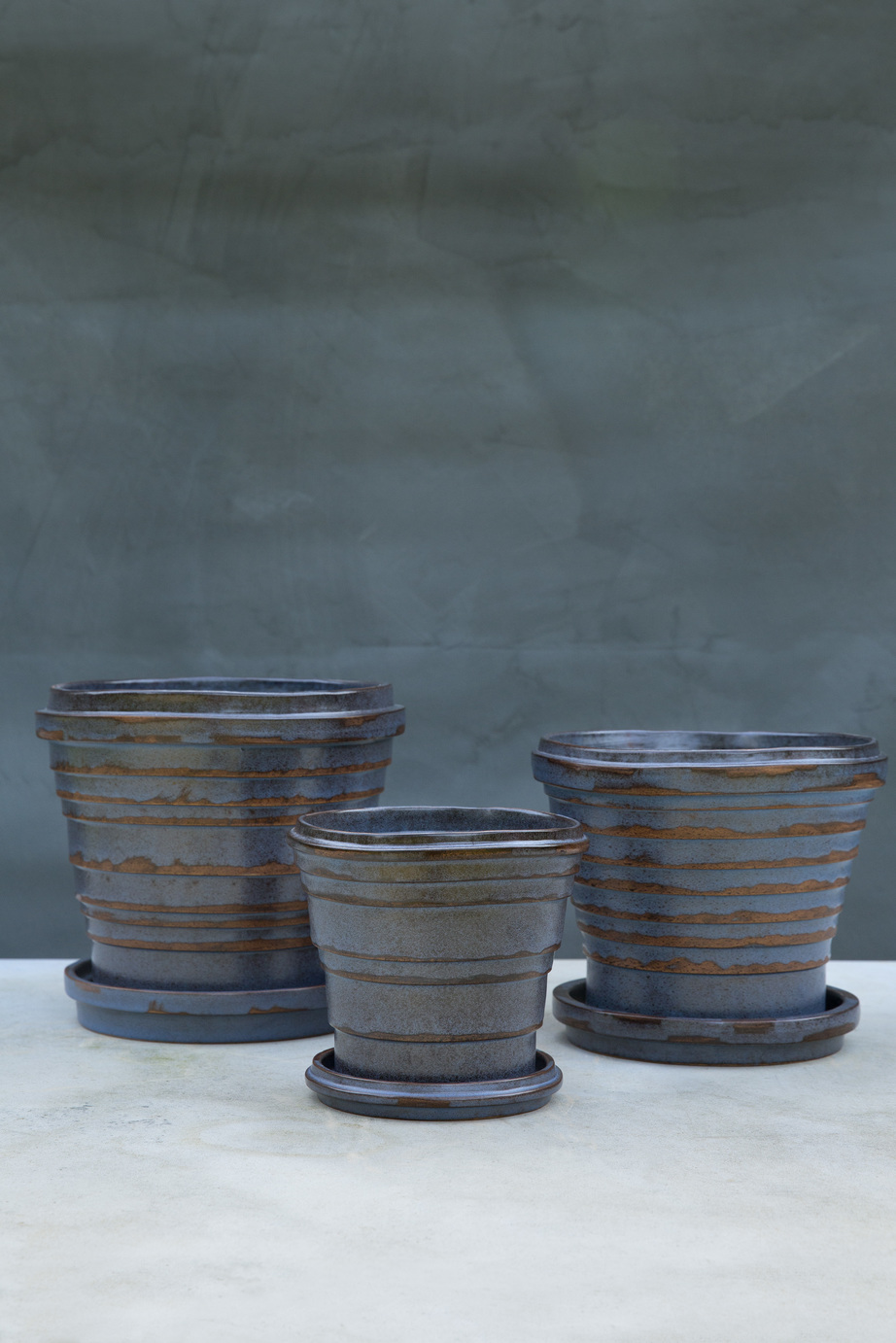 Three different sized pots, glazed blue/brown with saucers.