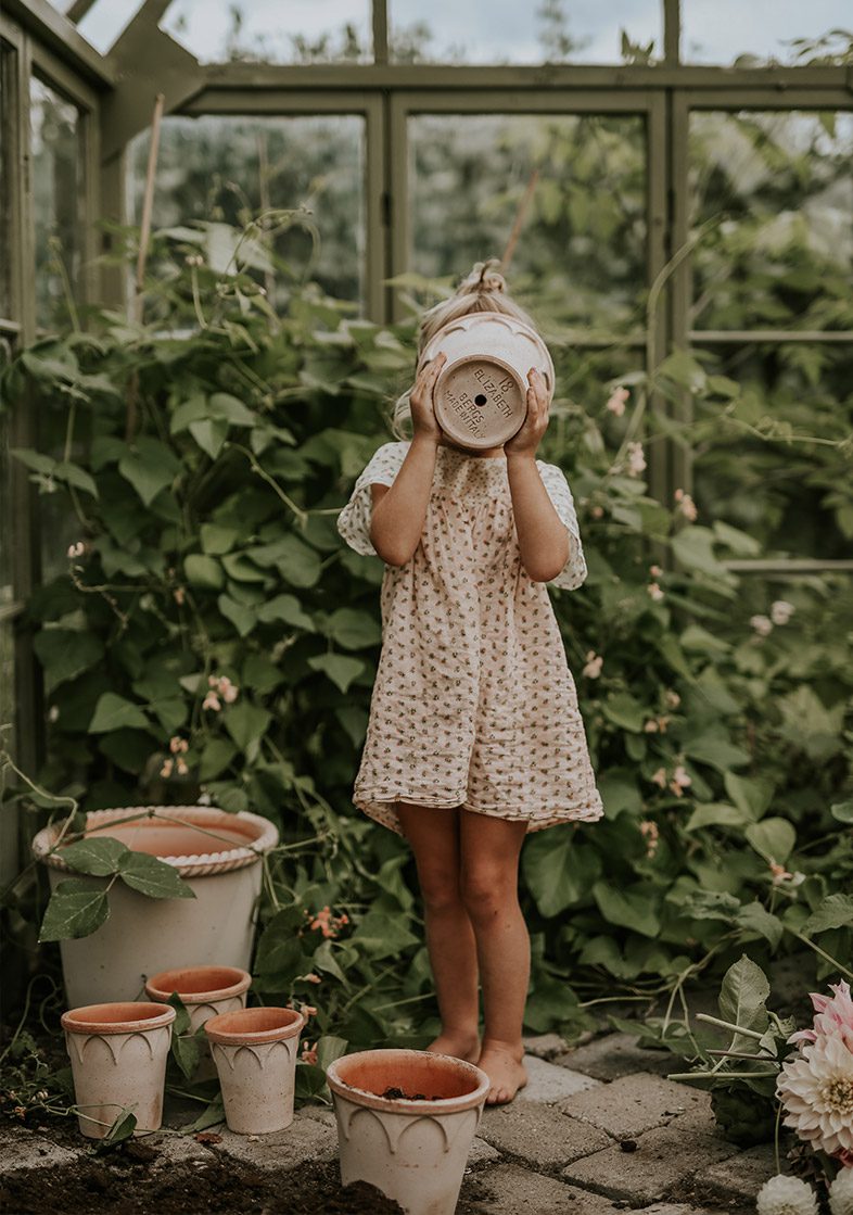 Girls holding a quality terracotta flower pot by Bergs Potter in front of her face inside a green conservatory. Photo: Anna Kubel.